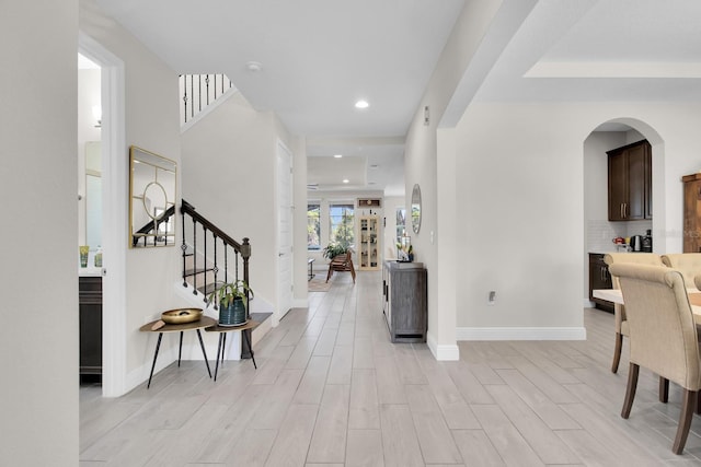 foyer featuring baseboards, light wood-type flooring, arched walkways, and stairs