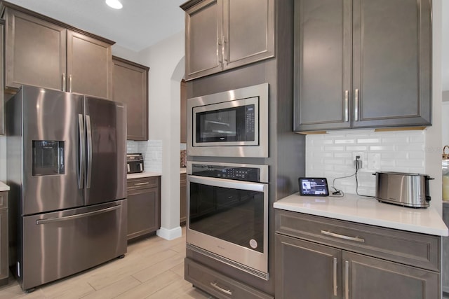 kitchen with tasteful backsplash, light wood-style flooring, appliances with stainless steel finishes, and light countertops