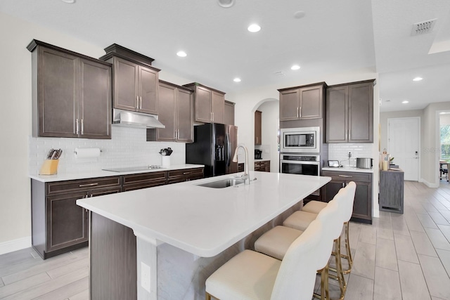 kitchen with a sink, visible vents, under cabinet range hood, black appliances, and arched walkways