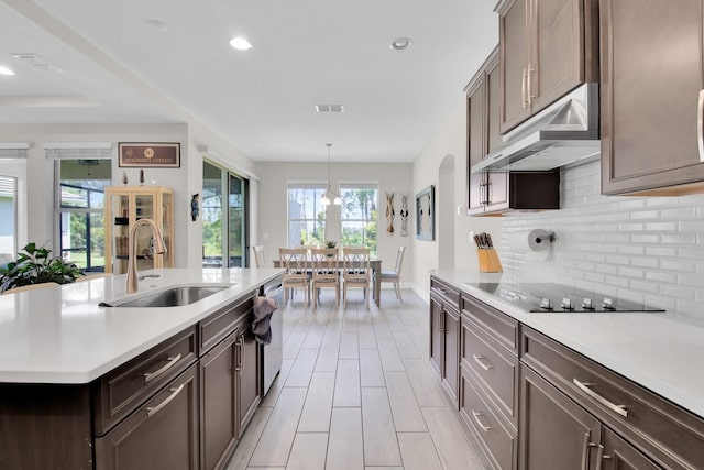 kitchen featuring stainless steel dishwasher, decorative backsplash, under cabinet range hood, light countertops, and a sink