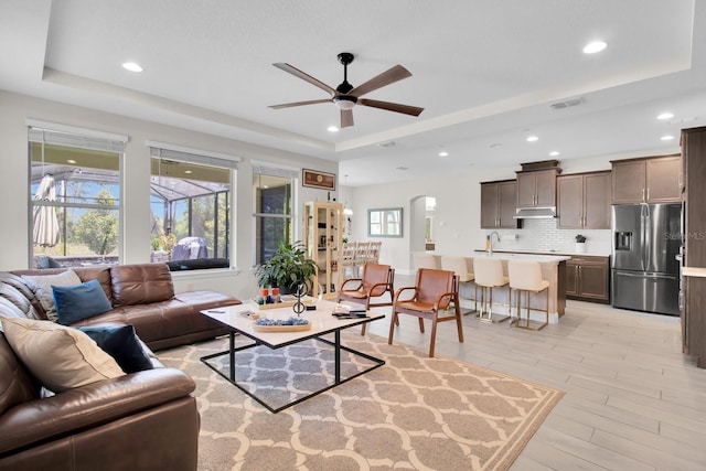 living room with light wood-style flooring, a raised ceiling, ceiling fan, visible vents, and recessed lighting
