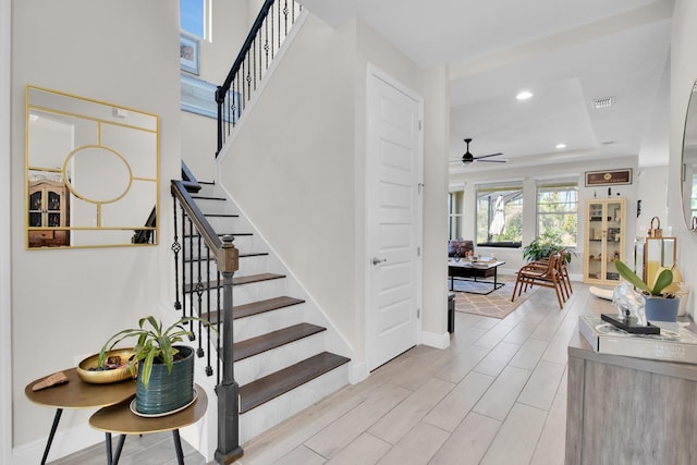stairway featuring ceiling fan, visible vents, a tray ceiling, baseboards, and recessed lighting