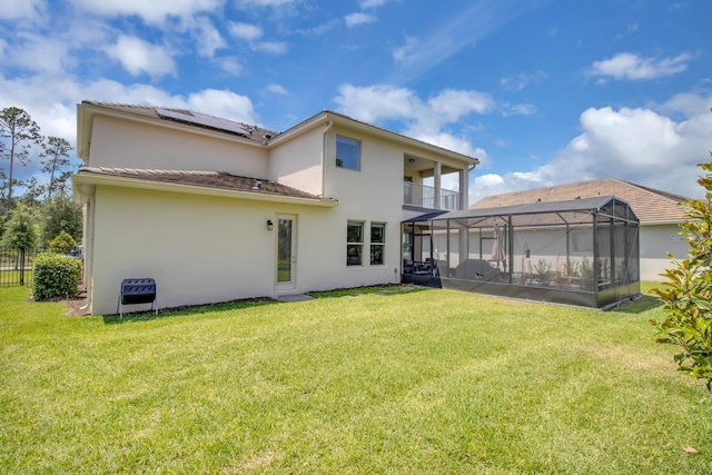 rear view of property featuring a yard, solar panels, stucco siding, and a balcony