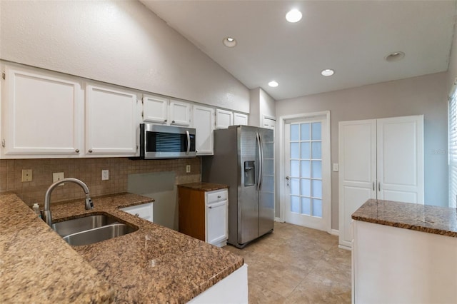kitchen with a sink, stainless steel appliances, decorative backsplash, white cabinetry, and lofted ceiling