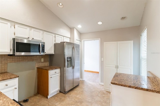 kitchen with dark stone countertops, decorative backsplash, stainless steel appliances, white cabinetry, and light tile patterned flooring