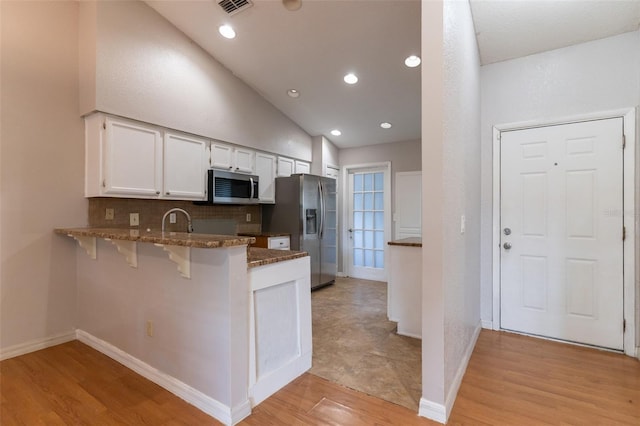 kitchen featuring dark stone countertops, decorative backsplash, stainless steel appliances, white cabinets, and a peninsula