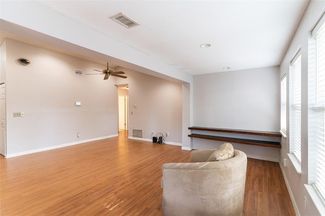 living room featuring a ceiling fan, visible vents, baseboards, and light wood-type flooring