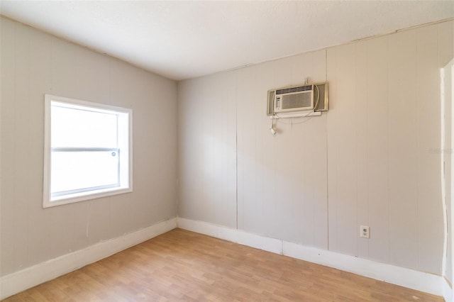 unfurnished room featuring baseboards, a wall unit AC, and light wood-type flooring