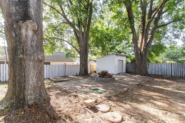 view of yard with a fenced backyard, an outdoor structure, a fire pit, a patio area, and a shed
