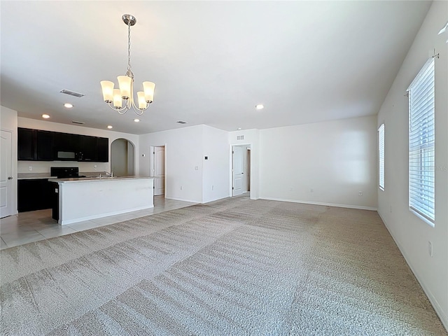 unfurnished living room with light colored carpet, visible vents, plenty of natural light, and a chandelier