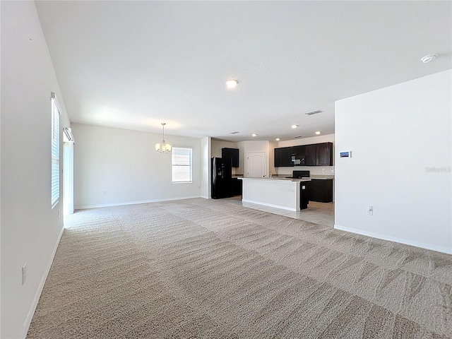 unfurnished living room with an inviting chandelier, baseboards, and light carpet