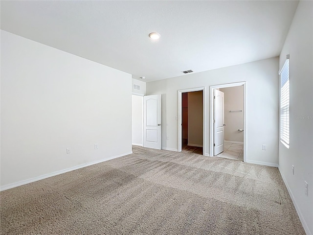 unfurnished bedroom with visible vents, a spacious closet, baseboards, and light carpet