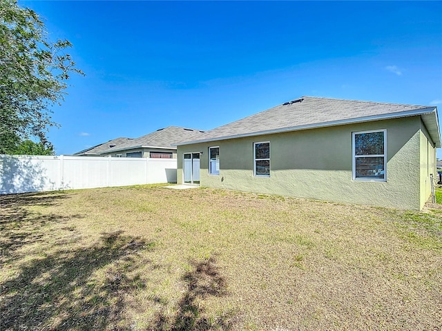 rear view of house with fence, stucco siding, and a lawn