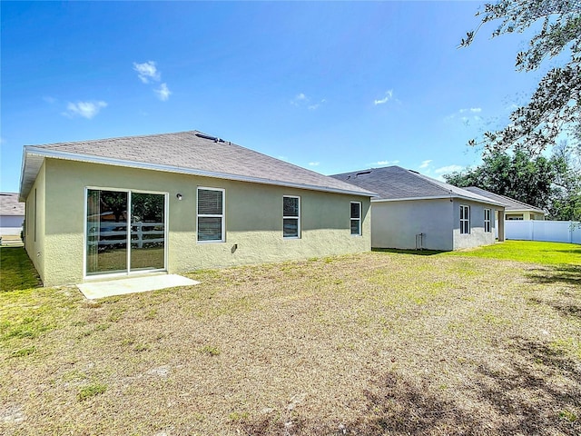 rear view of house featuring a lawn, stucco siding, and fence