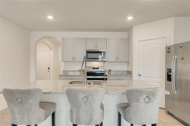 1535 Barberry Dr, Kissimmee, FL 34744 - kitchen with gray cabinets, appliances with stainless steel finishes, light tile patterned floors, light stone counters, and an island with sink