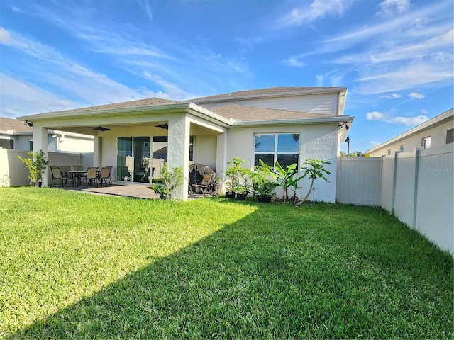 rear view of house with roof with shingles, a lawn, a patio area, a fenced backyard, and stucco siding