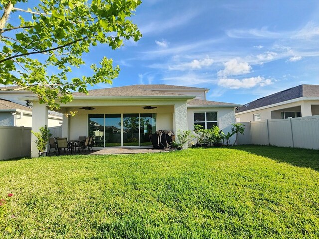 back of property with a yard, a ceiling fan, and stucco siding