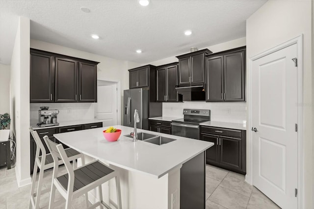 kitchen with tasteful backsplash, a sink, appliances with stainless steel finishes, a kitchen bar, and a center island with sink