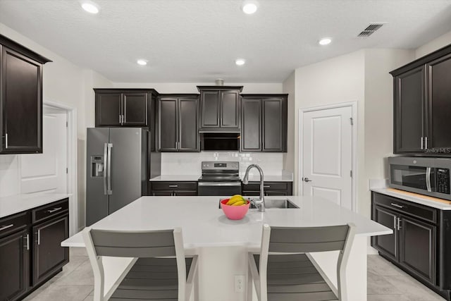 kitchen featuring a sink, visible vents, stainless steel appliances, light countertops, and a center island with sink