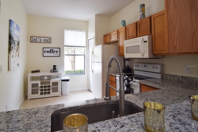 626 Verona Ave, Davenport, FL 33897 - kitchen with light stone countertops, brown cabinets, light tile patterned flooring, white appliances, and baseboards
