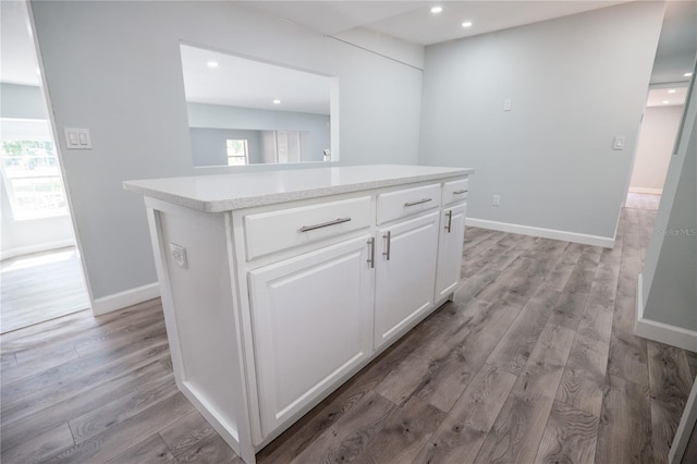interior space featuring white cabinets, light wood finished floors, a center island, recessed lighting, and baseboards