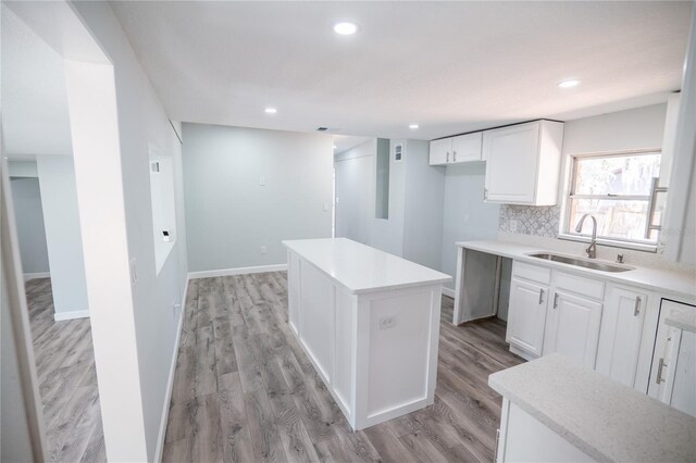 kitchen with backsplash, a center island, a sink, light wood-style floors, and white cabinetry