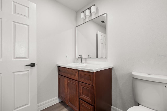 bathroom featuring vanity, toilet, visible vents, baseboards, and wood finished floors