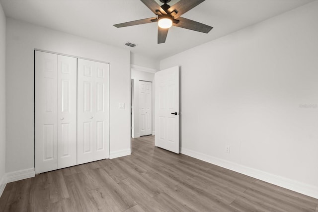 unfurnished bedroom featuring a closet, ceiling fan, visible vents, baseboards, and wood finished floors