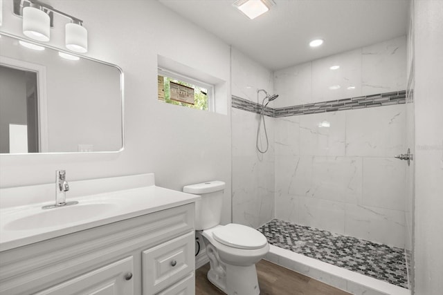 bathroom with toilet, wood finished floors, vanity, and tiled shower