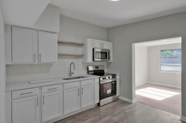 kitchen featuring light wood finished floors, a sink, open shelves, white cabinets, and appliances with stainless steel finishes