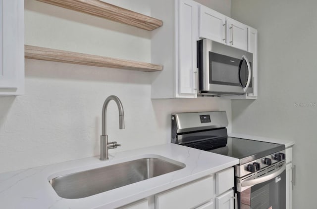 kitchen with light stone countertops, a sink, white cabinetry, and stainless steel appliances