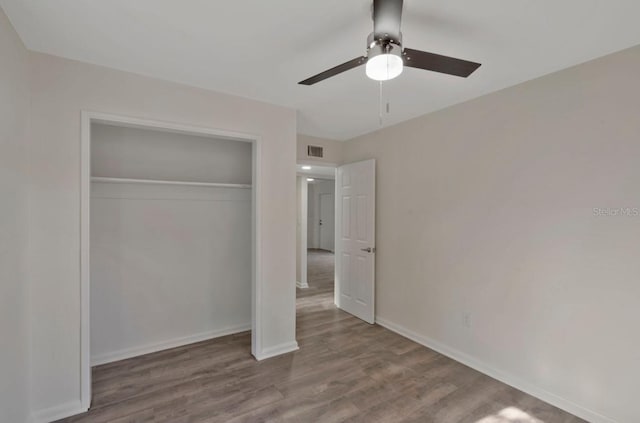 unfurnished bedroom featuring a closet, a ceiling fan, visible vents, baseboards, and wood finished floors