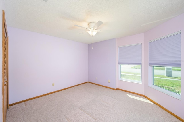 unfurnished room with a ceiling fan, a textured ceiling, light colored carpet, and baseboards