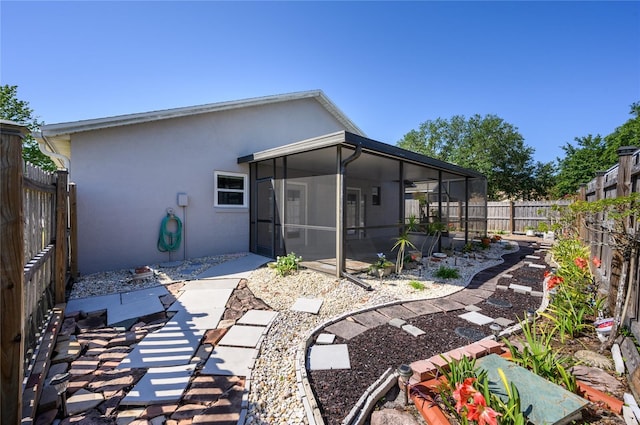 back of house featuring a sunroom, a fenced backyard, a patio area, and stucco siding