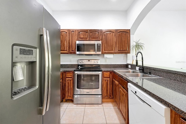 kitchen featuring brown cabinets, a sink, dark countertops, stainless steel appliances, and light tile patterned flooring