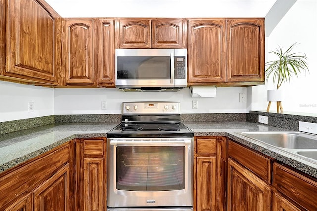 kitchen featuring dark countertops, brown cabinetry, a sink, and stainless steel appliances