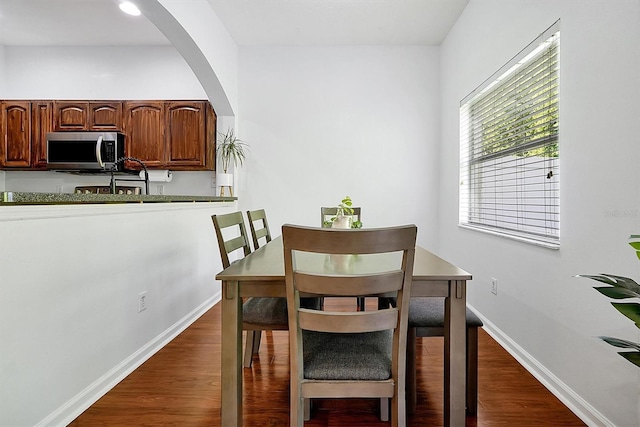 dining space with dark wood-type flooring, baseboards, and arched walkways