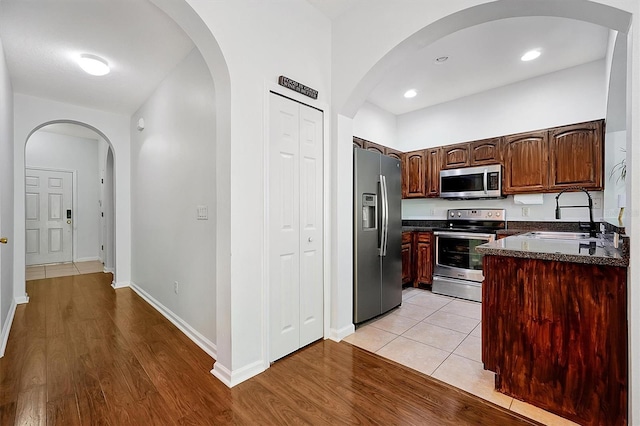 kitchen with appliances with stainless steel finishes, light wood-style floors, baseboards, and a sink