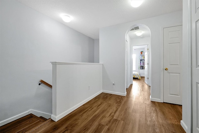hallway with wood finished floors, arched walkways, an upstairs landing, baseboards, and visible vents