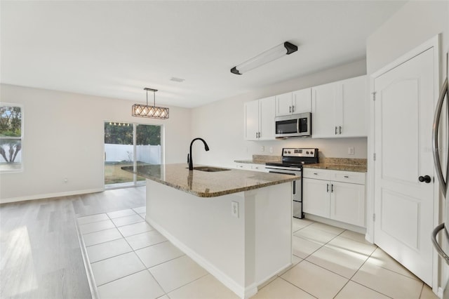 kitchen with a kitchen island with sink, white cabinets, a sink, stone counters, and stainless steel appliances