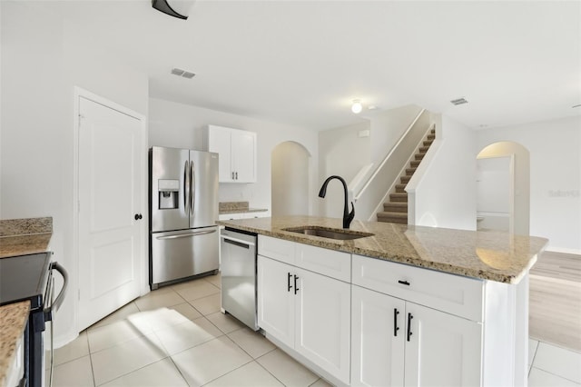 kitchen featuring light stone countertops, a sink, arched walkways, an island with sink, and stainless steel appliances