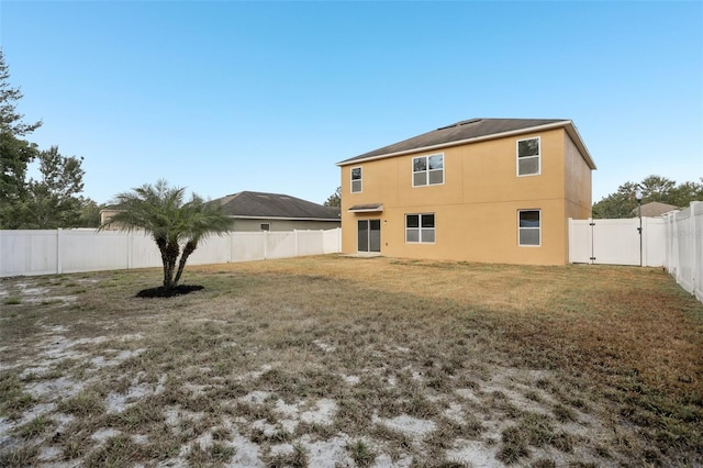 back of house with a fenced backyard, stucco siding, and a yard