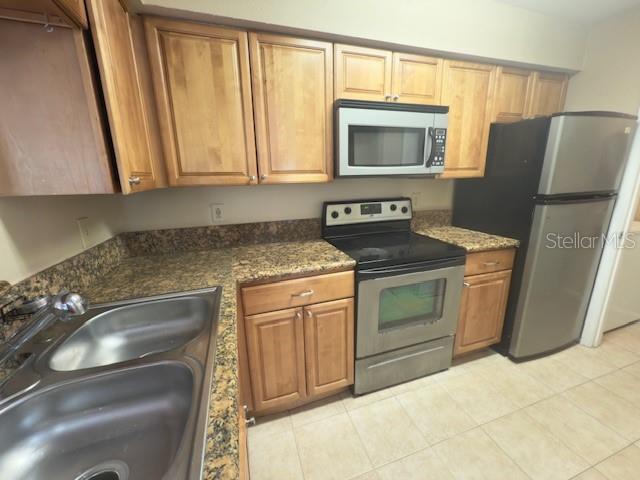 208 Afton Sq Unit 307, Altamonte Springs, FL 32714 - kitchen with stainless steel appliances, a sink, light tile patterned floors, brown cabinets, and dark stone counters