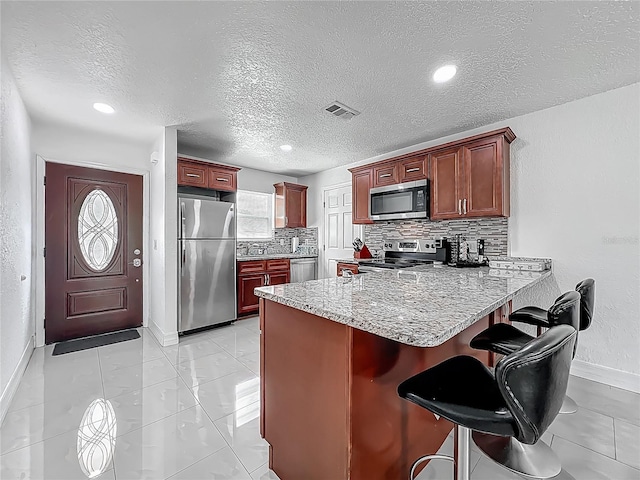 kitchen featuring tasteful backsplash, appliances with stainless steel finishes, visible vents, baseboards, and a peninsula