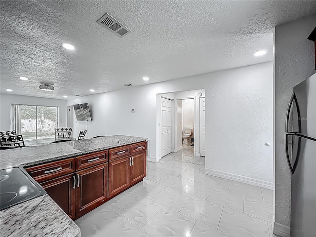 kitchen featuring a textured ceiling, freestanding refrigerator, dark brown cabinets, and visible vents