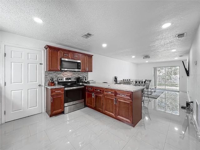 kitchen featuring stainless steel appliances, dark brown cabinets, a peninsula, and a textured ceiling