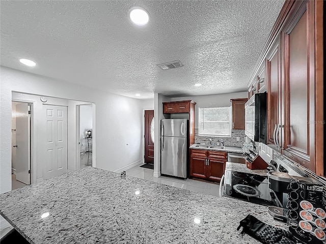 kitchen with appliances with stainless steel finishes, visible vents, dark brown cabinets, and light stone counters