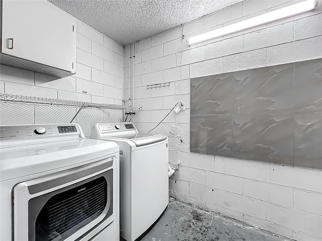 laundry room with concrete block wall, washer and dryer, cabinet space, and a textured ceiling