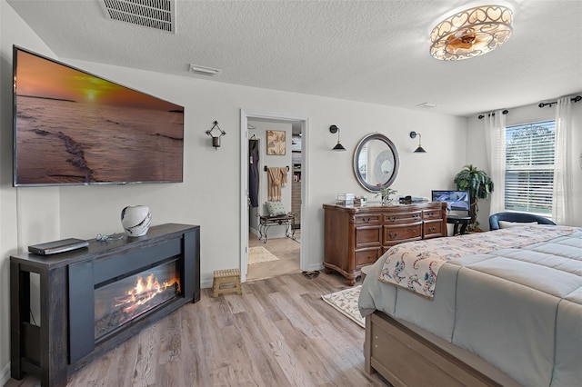 1220 Tahitian Sunrise Dr, Plant City, FL 33565 - bedroom with a textured ceiling, visible vents, a glass covered fireplace, and light wood finished floors