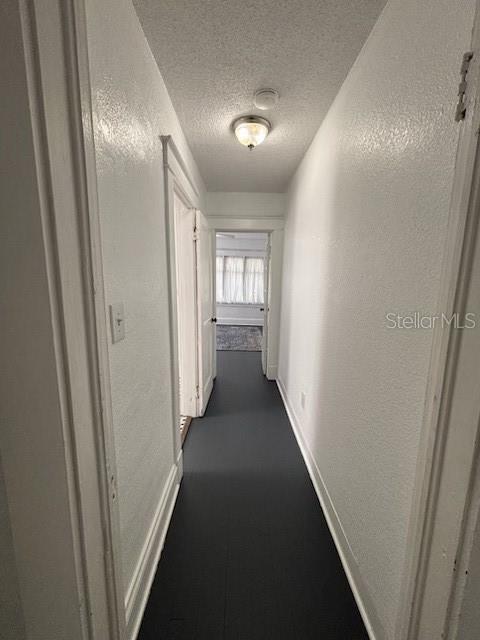 hall with baseboards and a textured ceiling